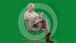 Portrait of aged bearded man on chroma key green screen background. Full shot of senior man sitting on a chair watching