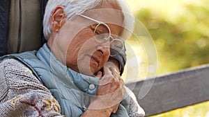 Portrait of aged Caucasian woman with glasses holding hand of her husband and closing eyes copy space park background