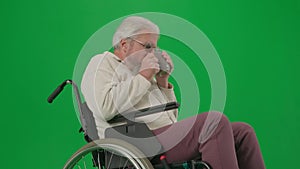 Portrait of aged disabled man on chroma key green screen. Close up senior man sitting in wheelchair feeling cold