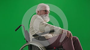 Portrait of aged disabled man on chroma key green screen. Close up senior man sitting in wheelchair rubbing his knee