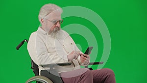 Portrait of aged disabled man on chroma key green screen. Close up senior man sitting in wheelchair surfing web on