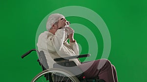 Portrait of aged disabled man on chroma key green screen. Close up senior man in wheelchair taking pictures on old film