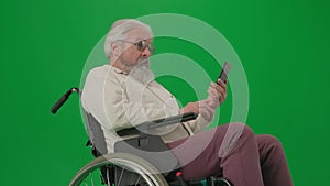 Portrait of aged disabled man on chroma key green screen. Close up senior man in wheelchair talking video call on