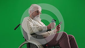 Portrait of aged disabled man on chroma key green screen. Close up senior man in wheelchair typing card number in