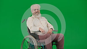 Portrait of aged disabled man on chroma key green screen. Elderly man sits in wheelchair and smiles at the camera.