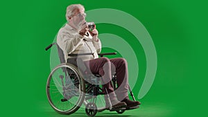 Portrait of aged disabled man on chroma key green screen. Full shot senior man in wheelchair takes photos on old film