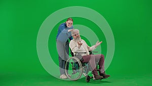 Portrait of aged disabled man on chroma key green screen. Girl granddaughter carries senior man on a wheelchair and