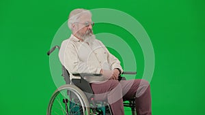 Portrait of aged disabled man on chroma key green screen. Senior man sitting in wheelchair and looking directly at the