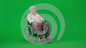 Portrait of aged disabled man on chroma key green screen. Senior man sitting in wheelchair and looking sideways at the