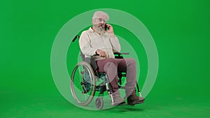 Portrait of aged disabled man on chroma key green screen. Senior man sitting in wheelchair and talking on smartphone.