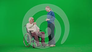 Portrait of aged disabled man on chroma key green screen. Senior man in wheel chair and young girl assistant caregiver