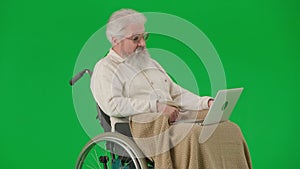 Portrait of aged disabled man on chroma key green screen. Senior man in wheelchair covered in plaid talking video call