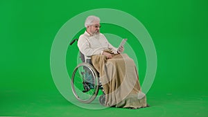 Portrait of aged disabled man on chroma key green screen. Senior man in wheelchair covered in plaid talking video call
