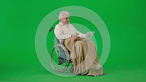 Portrait of aged disabled man on chroma key green screen. Senior man in wheelchair covered in plaid talking video call