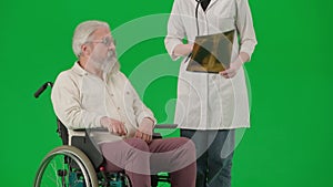 Portrait of aged disabled man on chroma key green screen. Senior man in wheelchair with doctor looking at lungs x-ray