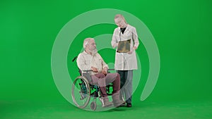 Portrait of aged disabled man on chroma key green screen. Senior man in wheelchair with doctor looking at lungs x-ray
