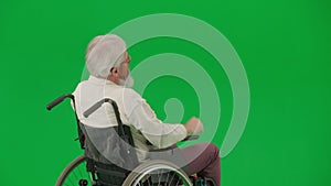 Portrait of aged disabled man on chroma key green screen. Senior man in wheelchair giving directions and gesturing with
