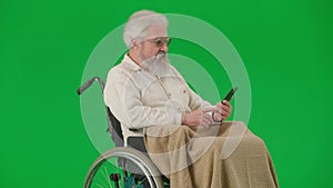 Portrait of aged disabled man on chroma key green screen. Senior man in wheelchair in plaid talking video call on