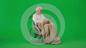 Portrait of aged disabled man on chroma key green screen. Senior man in wheelchair in plaid talking video call on