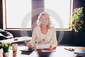 Portrait of aged lady hold papers use calculator wear white cardigan loft interior office house indoors
