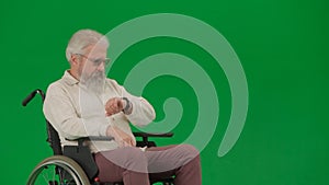Portrait of aged man on chroma key green screen background. Elderly man sitting in a wheelchair and looking at the clock