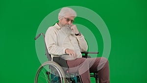 Portrait of aged man on chroma key green screen background. Elderly man sitting in a wheelchair, thoughtfully propping