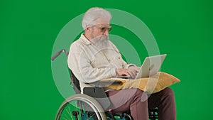 Portrait of aged man on chroma key green screen background. Senior man sitting in wheelchair and holding laptop on