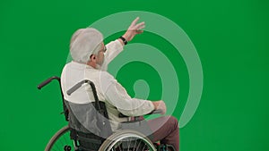 Portrait of aged man on chroma key green screen background. Senior man sitting in wheelchair shows directions and