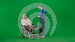 Portrait of aged man on chroma key green screen background. Young girl standing and chatting with senior man granddad on