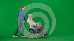 Portrait of aged man on chroma key green screen background. Young girl walks and carries senior man granddad on a
