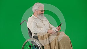 Portrait of aged man isolated on chroma key green screen background. Senior man in wheelchair covered by plaid holding