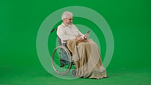 Portrait of aged man isolated on chroma key green screen background. Senior man in wheelchair covered by plaid holding