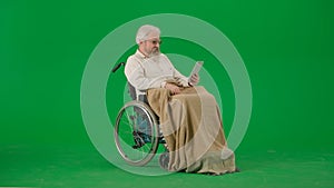 Portrait of aged man isolated on chroma key green screen background. Senior man in wheelchair covered by plaid holding