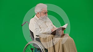 Portrait of aged man isolated on chroma key green screen background. Senior man in wheelchair covered by plaid reading