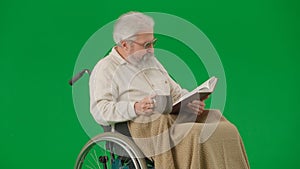 Portrait of aged man isolated on chroma key green screen background. Senior man in wheelchair covered by plaid reading