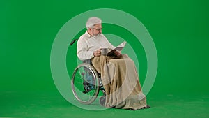 Portrait of aged man isolated on chroma key green screen background. Senior man in wheelchair covered by plaid reading