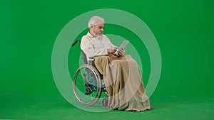 Portrait of aged man isolated on chroma key green screen background. Senior man in wheelchair covered by plaid swiping