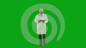 Portrait of aged man medic on chroma key green screen. Senior doctor in uniform walking holding reading medical card