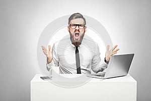 Portrait of aggressive businessman in white shirt and black tie are sitting in office and having bad mood with raised arms looking