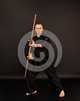 Portrait of aikido sensei master with black sensei belt in taekwondo kimono with bokken on black background. Traditional samurai