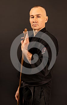 Portrait of aikido sensei master with black sensei belt in taekwondo kimono with bokken on black background. Traditional samurai