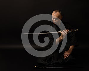 Portrait of aikido sensei master with black sensei belt in taekwondo kimono witn sword katana on black background. Traditional