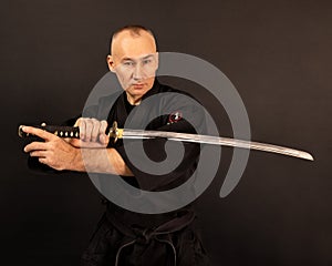 Portrait of aikido sensei master with black sensei belt in taekwondo kimono witn sword katana on black background. Traditional