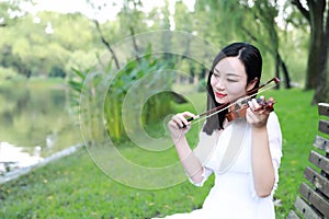 Portrait of Aisan Chinese girl woman artist play violin in nature park forest enjoy leisure time performance outdoor lake bench