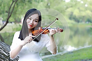 Portrait of Aisan Chinese girl woman artist play violin in nature park forest enjoy leisure time performance outdoor lake forest