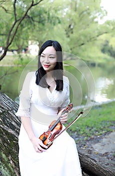 Portrait of Aisan Chinese girl woman artist play violin in nature park forest enjoy leisure time performance outdoor lake forest