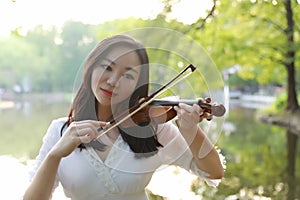 Portrait Aisan Chinese girl woman artist play violin in nature park forest enjoy leisure time performance outdoor lake sunrise