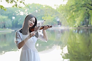 Portrait of Aisan Chinese girl woman artist play violin in nature park forest enjoy leisure time performance outdoor lake sunset