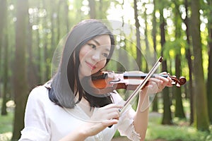 Portrait of Aisan Chinese girl woman artist play violin in nature park forest enjoy leisure time performance outdoor park sunshine