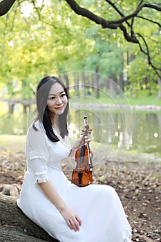 Portrait of Aisan Chinese girl woman play violin in nature park garden under a tree enjoy leisure time performance outdoor in park